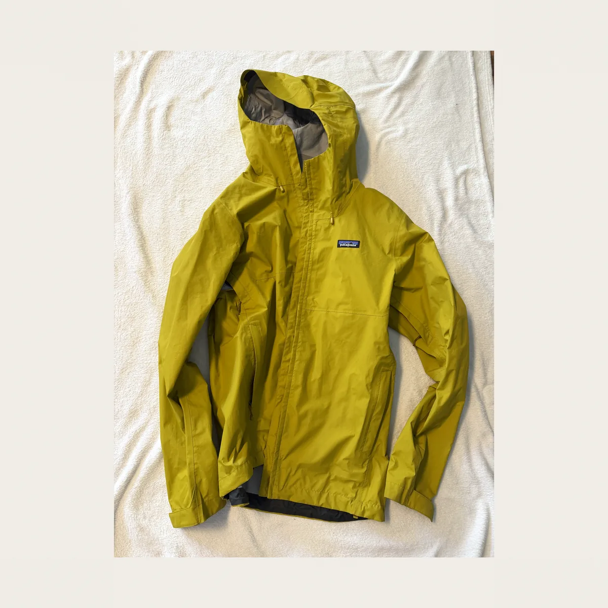 Gelbe Hardshelljacke mit Kapuze auf hellem Untergrund ausgebreitet
